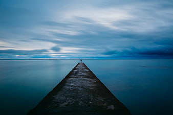 Solitary Figure on Pier at Dusk with Blue Sky
