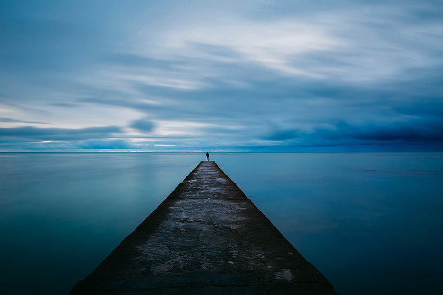 Solitary Figure on Pier at Dusk with Blue Sky