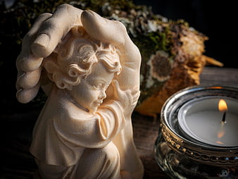 Wooden Angel Statue and Lit Candle in Dark Setting