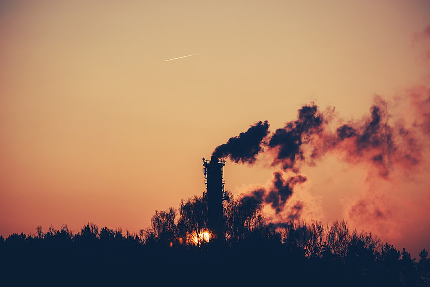 Industrial smokestack silhouette against orange sunset sky