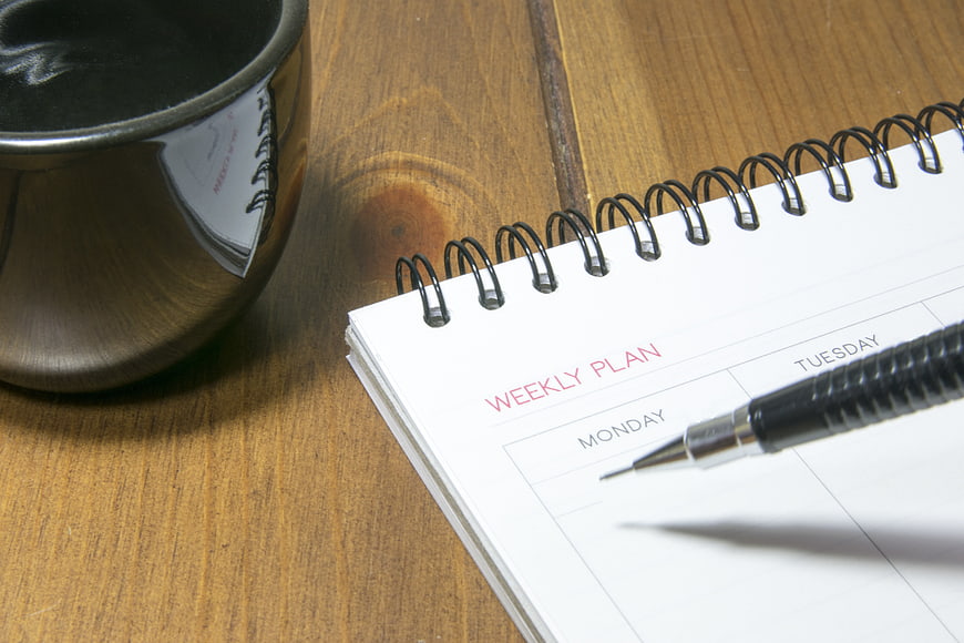 Weekly planner notebook with pen and coffee cup on wooden desk
