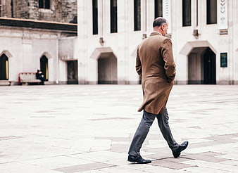 Senior man in brown coat walking in city square