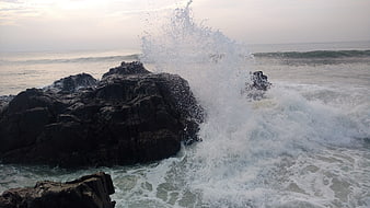 Powerful ocean wave crashing against dark coastal rocks