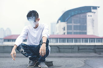 Young man smoking on urban rooftop with city background