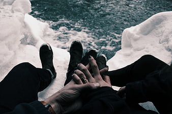 Couple holding hands sitting on snowy riverbank