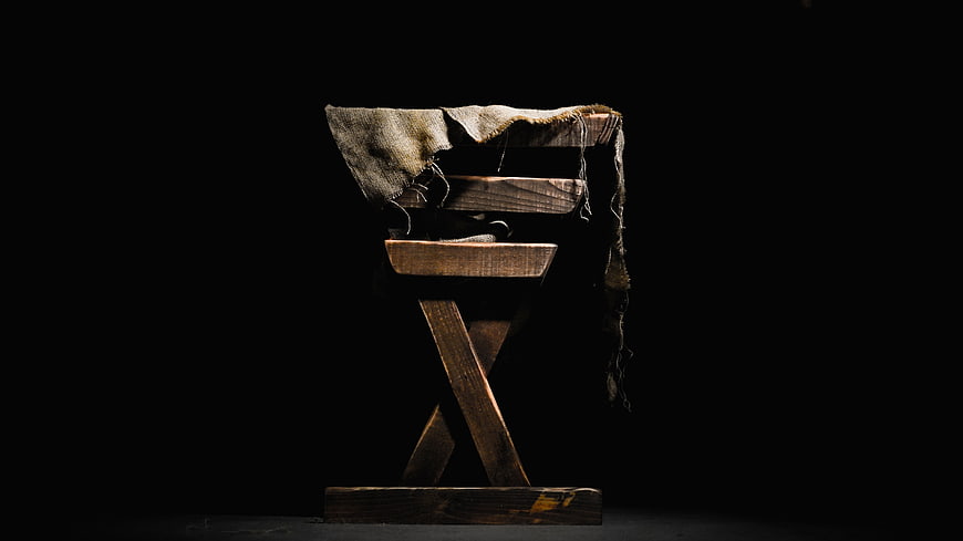 Dark moody wooden stool with burlap cloth on black background