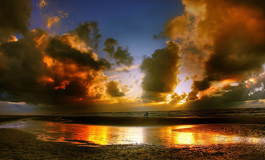 Dramatic sunset over ocean with silhouetted couple on beach