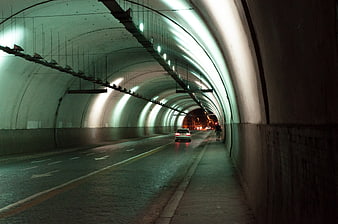 Car driving through illuminated tunnel with pedestrian walking