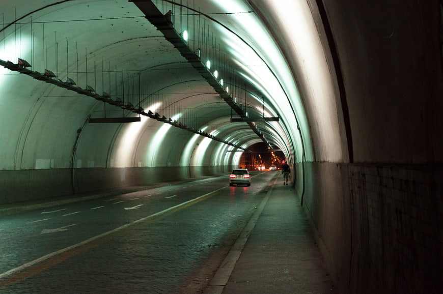 Car driving through illuminated tunnel with pedestrian walking