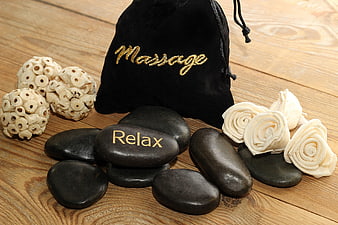 Spa massage stones with relax text and black velvet bag on wooden surface