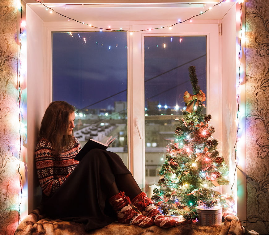 Woman Reading by Christmas Tree in Window Nook