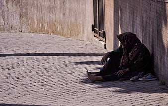 Elderly woman sitting alone on a cobblestone street corner