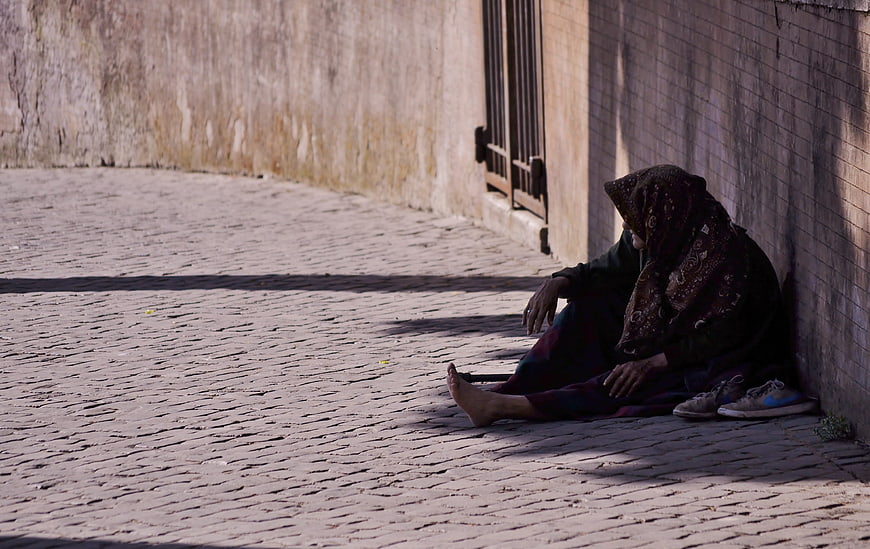 Elderly woman sitting alone on a cobblestone street corner