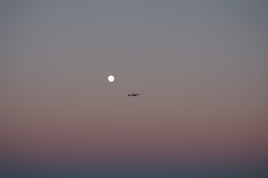 Airplane Flying Past Moon in Twilight Sky