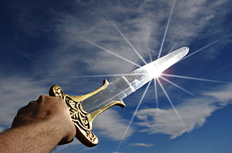 Hand holding golden sword against blue sky with sun flare