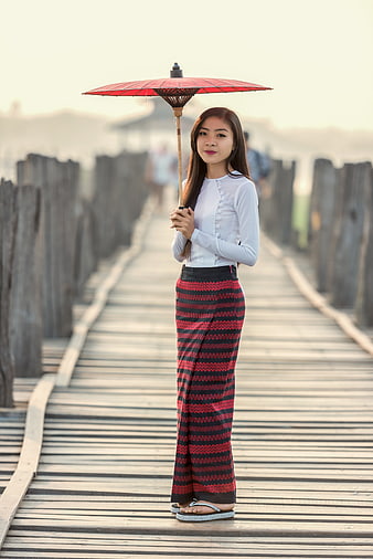 Woman in Traditional Attire Holding Red Umbrella on Wooden Bridge