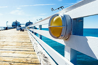 Yellow pier light fixture on white wooden railing overlooking blue ocean