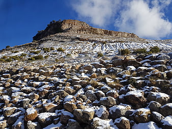 Snow-covered rocky mountain slope under blue sky