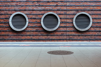 Modern brick wall with three circular vents and sidewalk