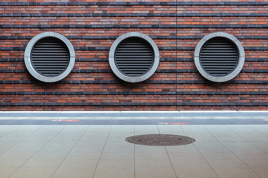 Modern brick wall with three circular vents and sidewalk