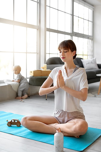 Mother meditating at home with baby playing in background