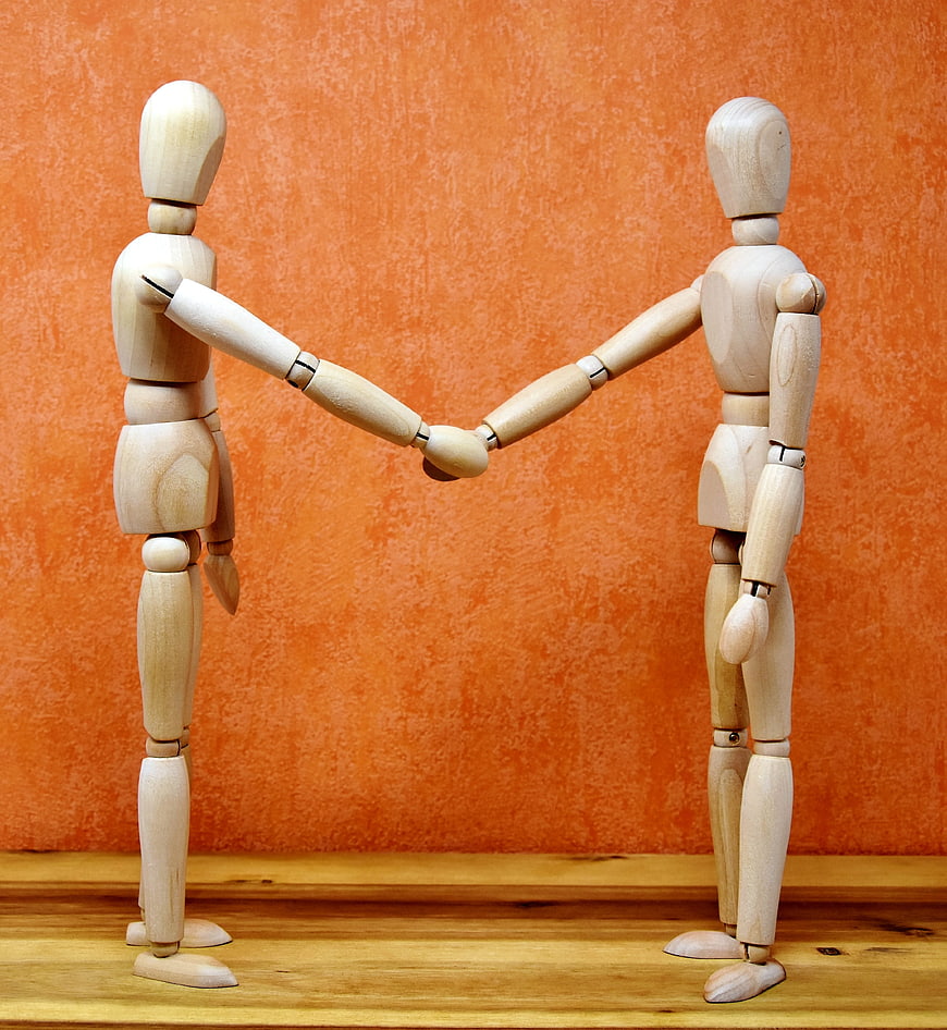 Wooden Mannequins Shaking Hands on Orange Background
