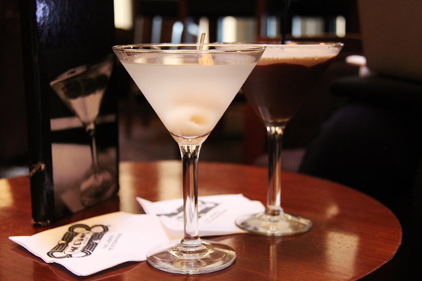 Two elegant cocktails in martini glasses on a wooden bar table