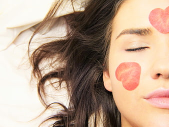 Woman with heart-shaped facial masks relaxing on white bed