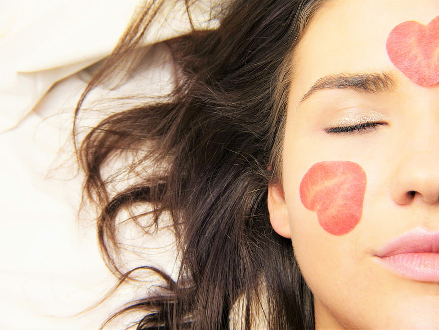 Woman with heart-shaped facial masks relaxing on white bed