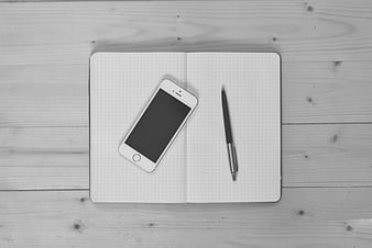 Black and White Flat Lay of Smartphone, Pen, and Grid Notebook on Wood