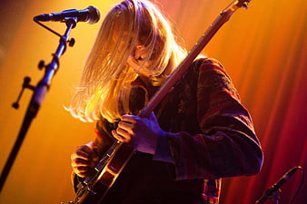 Female musician playing electric guitar on stage with warm orange lighting
