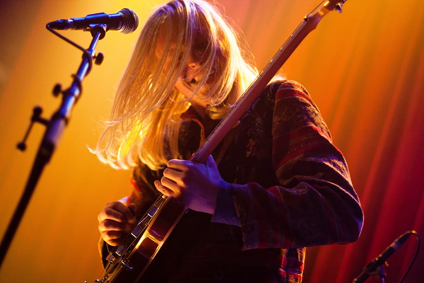 Female musician playing electric guitar on stage with warm orange lighting
