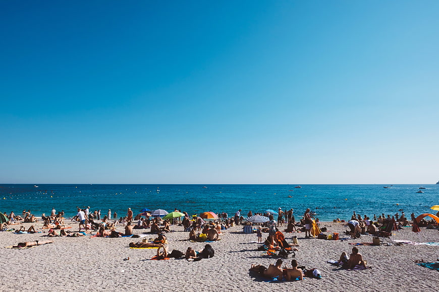 Crowded pebble beach with blue sky and ocean horizon