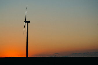 Silhouette of wind turbine against orange sunset sky