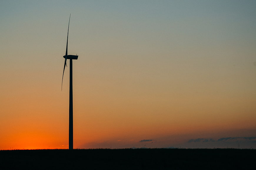 Silhouette of wind turbine against orange sunset sky