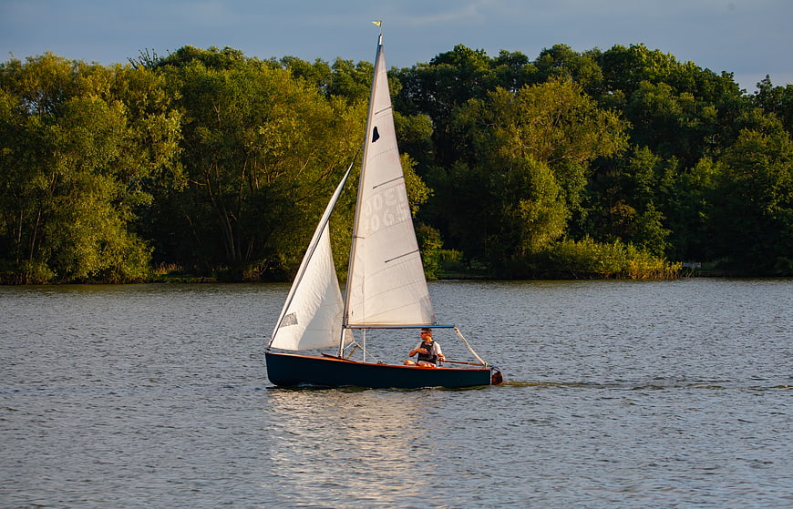 Man sailing small boat on calm lake with trees