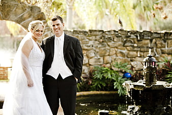 Happy Bride and Groom Standing by Garden Fountain