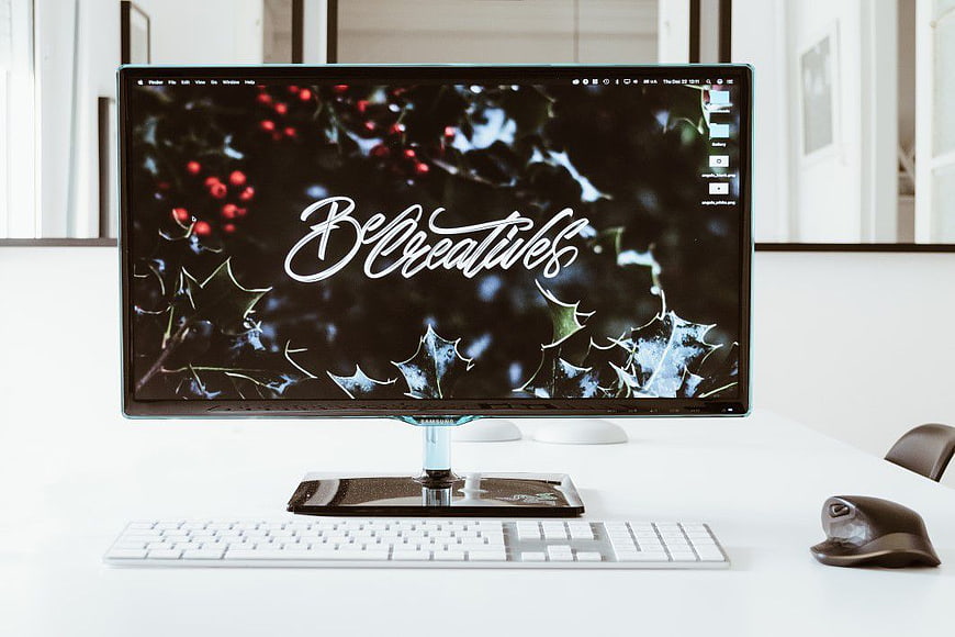 Minimalist white desk with computer monitor displaying Be Creative text