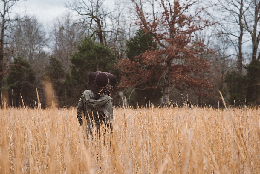 Woman with large hat walking through tall dry grass field