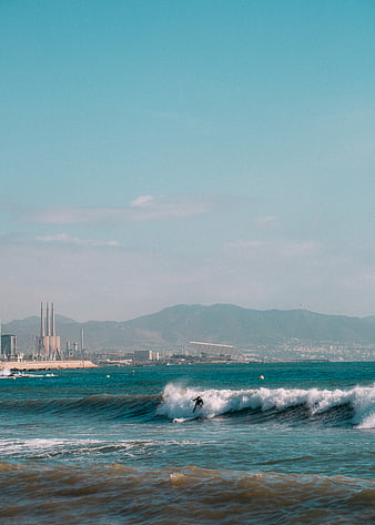 Surfer riding wave with industrial cityscape background