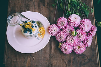 Overhead view of yogurt with blueberries and pink flowers on wood