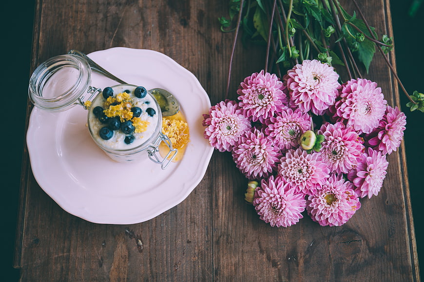 Overhead view of yogurt with blueberries and pink flowers on wood