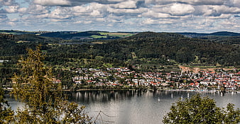 Panoramic view of a lakeside village with forested hills