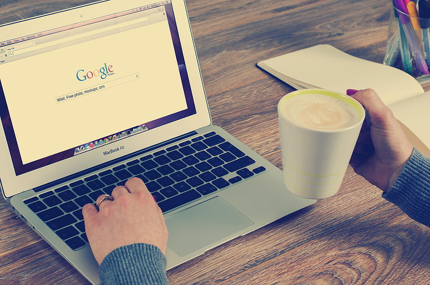 Woman typing on laptop with coffee cup on wooden desk