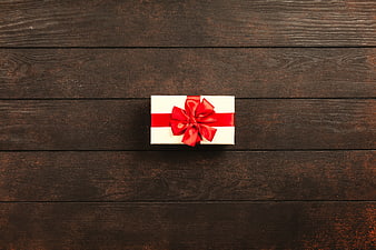 White Gift Box with Red Bow on Dark Wood Background