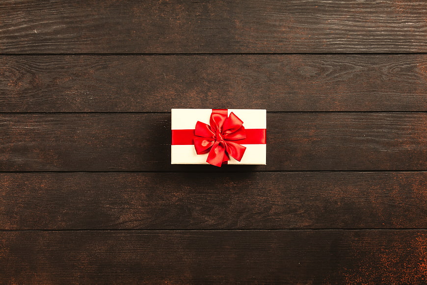 White Gift Box with Red Bow on Dark Wood Background