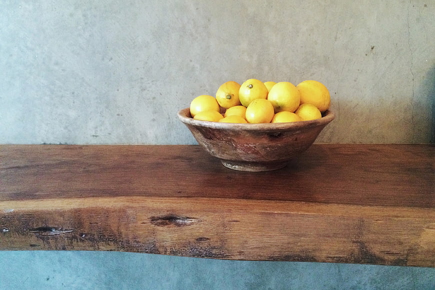 Rustic wooden bowl of lemons on a shelf