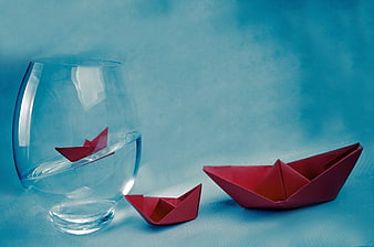 Red paper boats floating in water glass on blue background