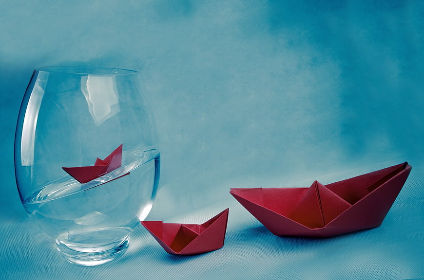 Red paper boats floating in water glass on blue background