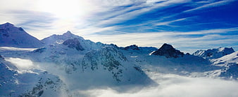 Panoramic View of Snow-Covered Mountain Peaks Above Clouds
